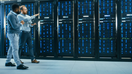 Two data center technicians walking past illuminated server racks.